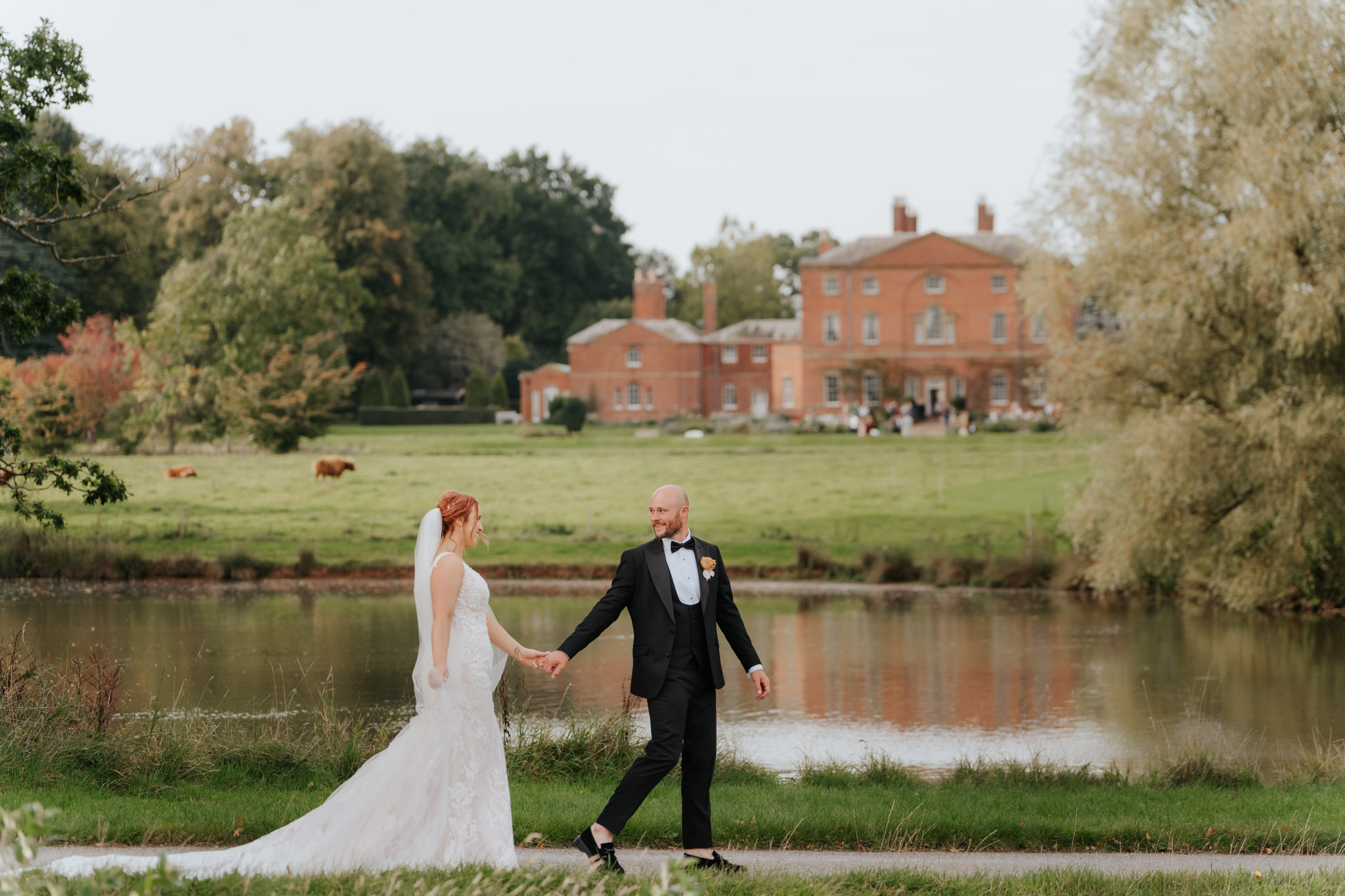 Groom in black tuxedo leads bride on a walk past Norwood Park