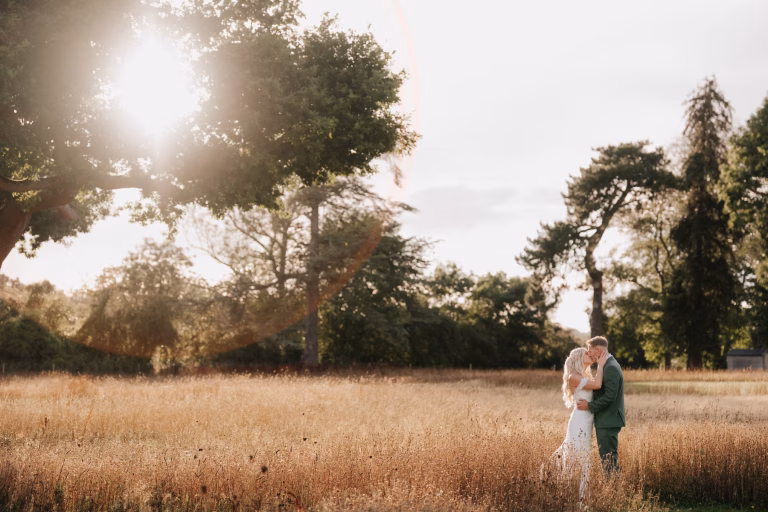 Sunset wedding photo with bride & groom kissing in a field at St tewdrics house, wales