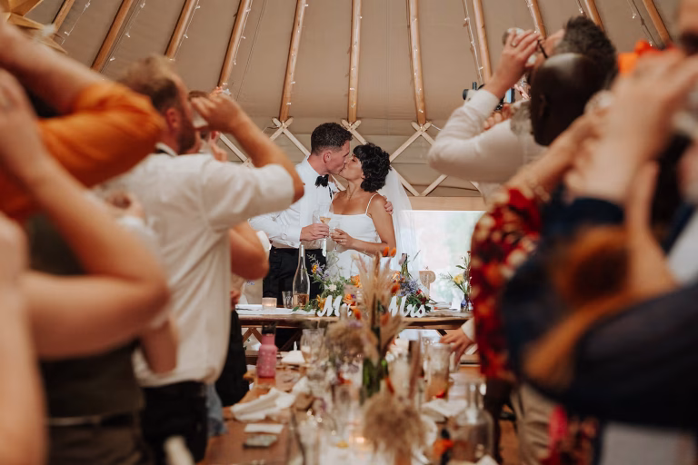 Bride & Groom kissing whilst guests raise a glass to toast their wedding day